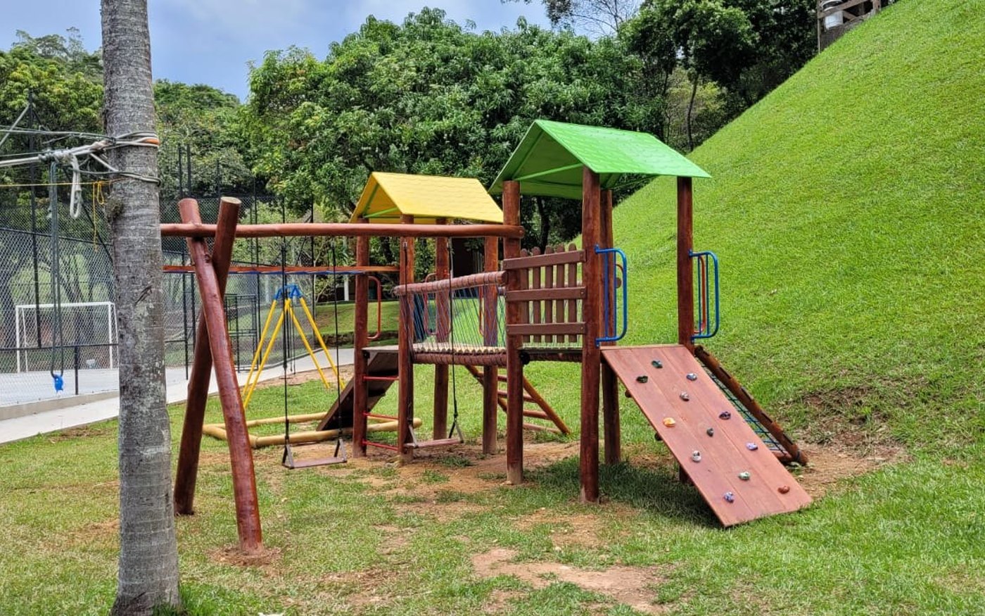 Playground de madeira de eucalipto instalado em área gramada, com rampa de escalada e balanços