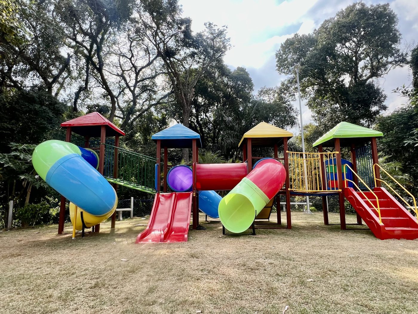 Conjunto de playground com torres, tobogãs e escorregadores instalado em área externa arborizada